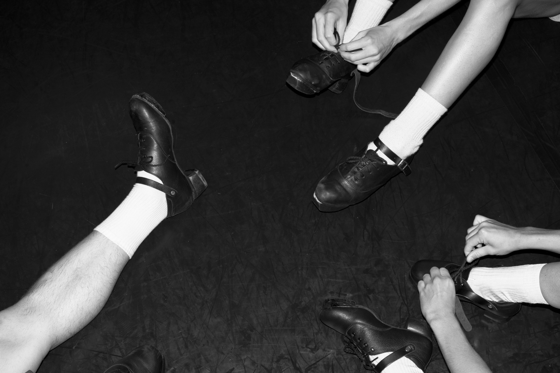 Black-and-white overhead view of dancers fastening percussive dance shoes.
