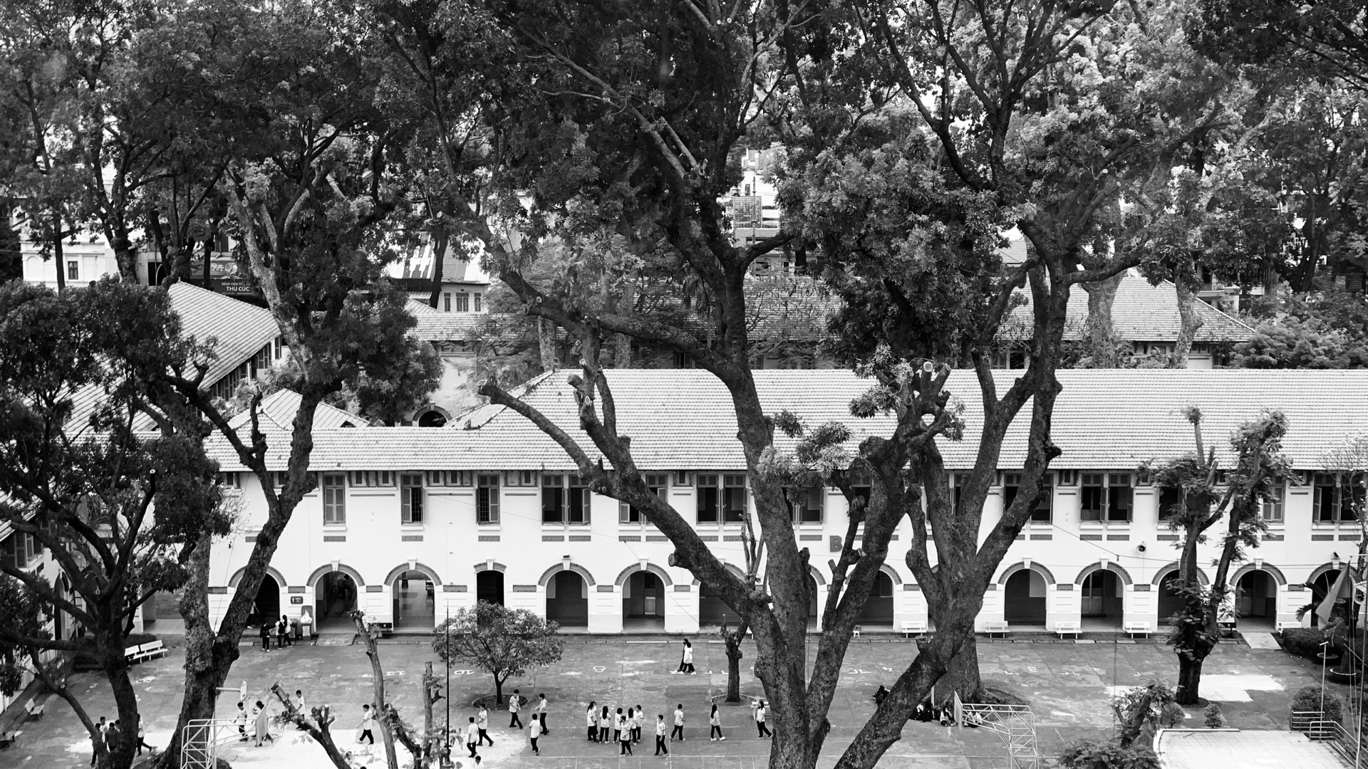 A black-and-white view of a Saigon courtyard framed by mature trees.