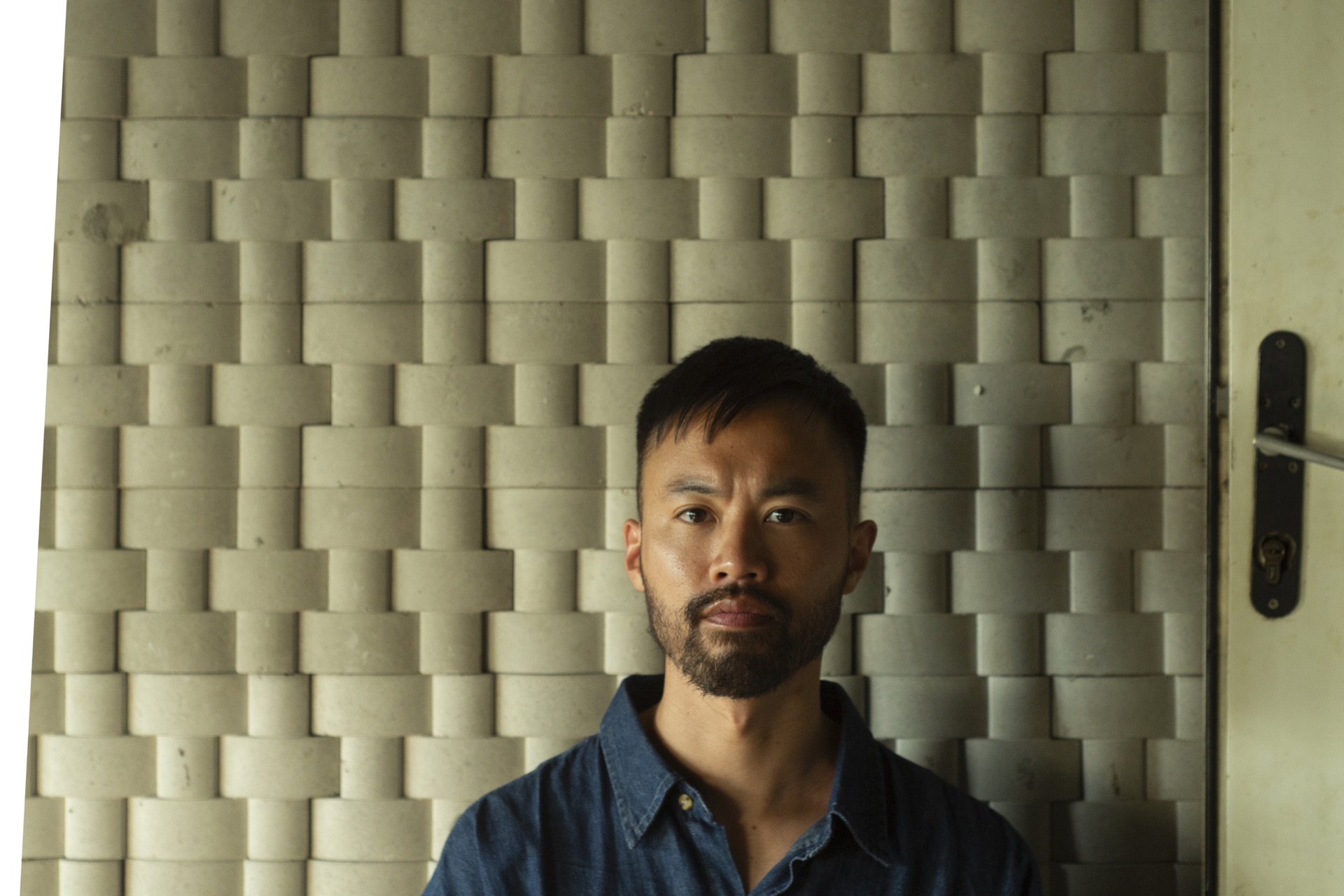 Portrait of Tony Trinh Tran in front of a sculptural concrete wall.
